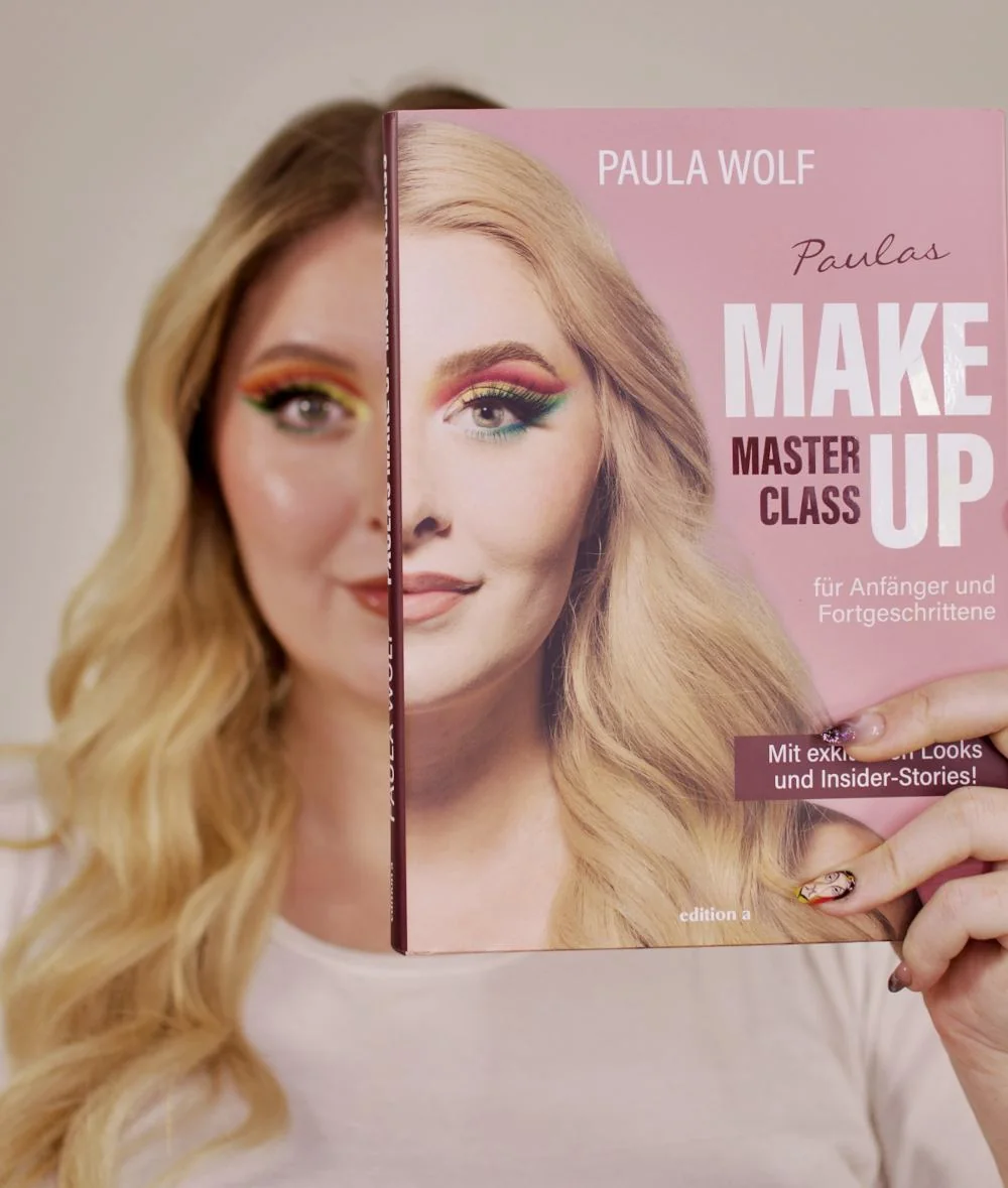 Paula Wolf hält ihr Buch Paulas Make-up-Masterclass vor ihr Gesicht